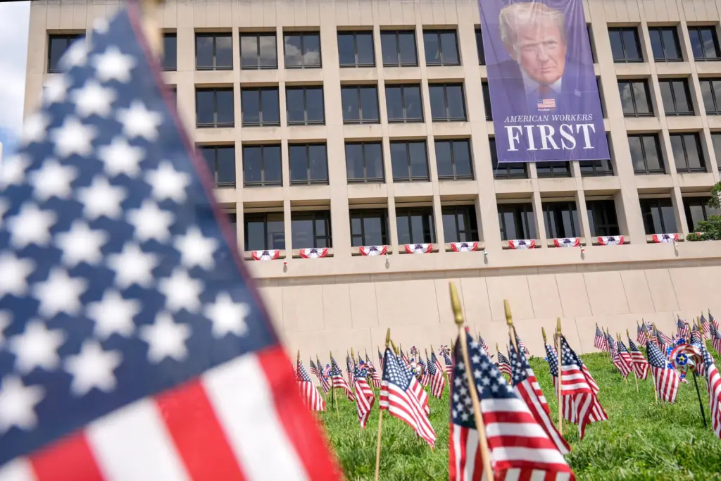 Flags are pictured in grass near a banner depicting a...