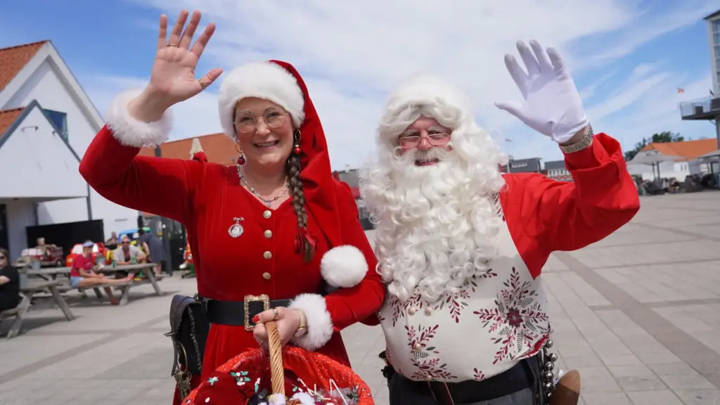 A Santa Claus and Christmas elf performer wave to the camera.