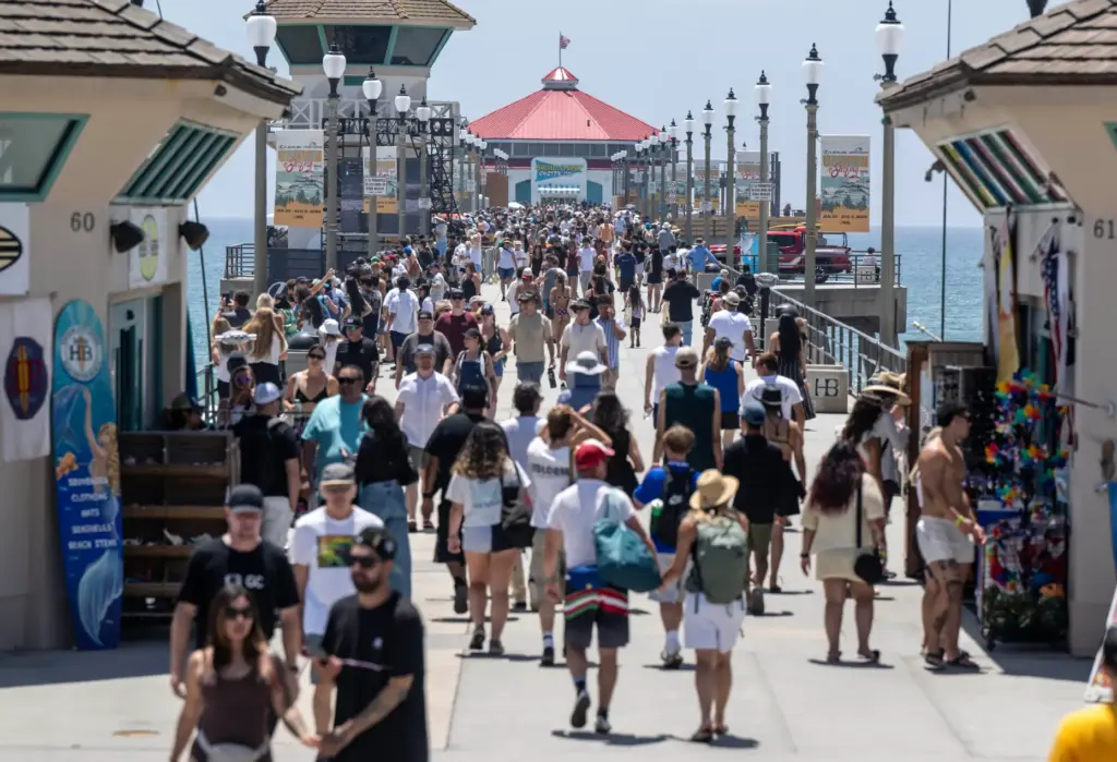Hundreds of surf fans and beachgoers walk along the pier,...