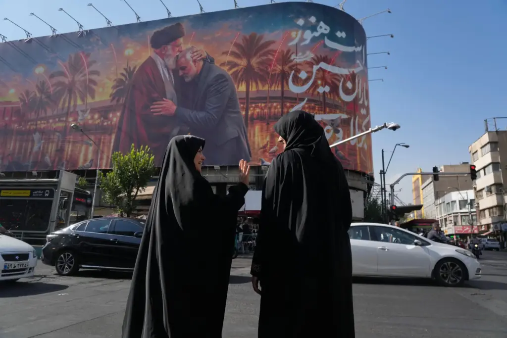Women talk in front of a banner with graphic depicting...