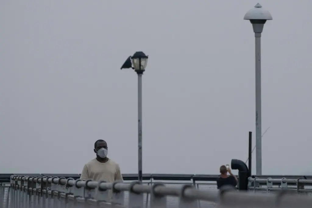 A person wearing a mask walks on a pier as smoke from wildfires blankets the sky.