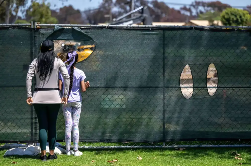 A pair of parkgoers peaks through a hole in the...