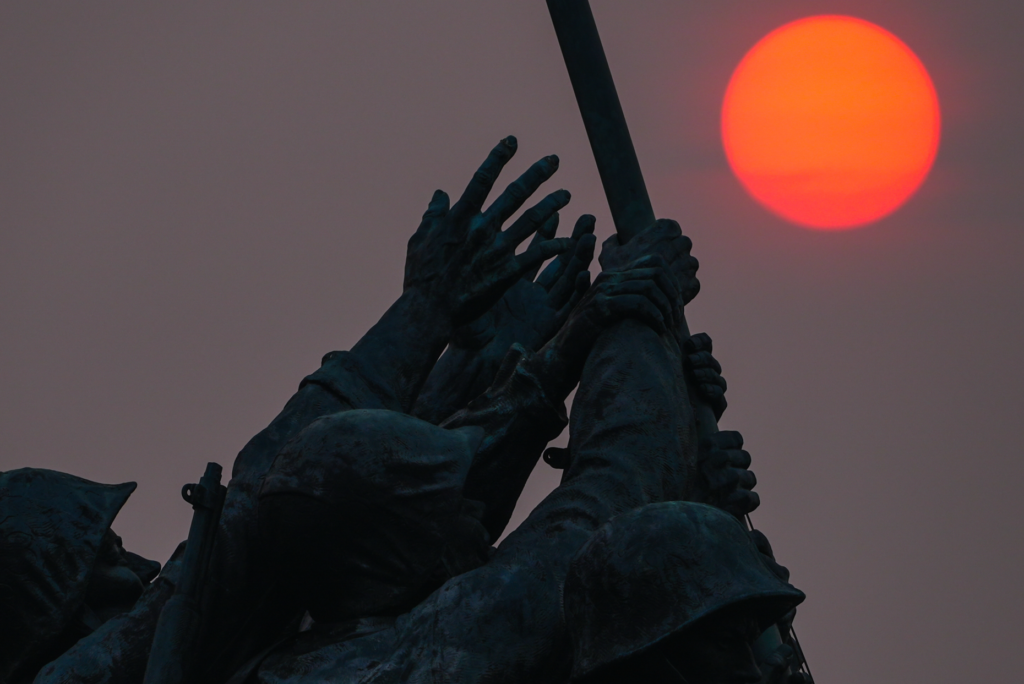 The sun is obscured by wildfire smoke as it rises behind the Marine Corps War Memorial.