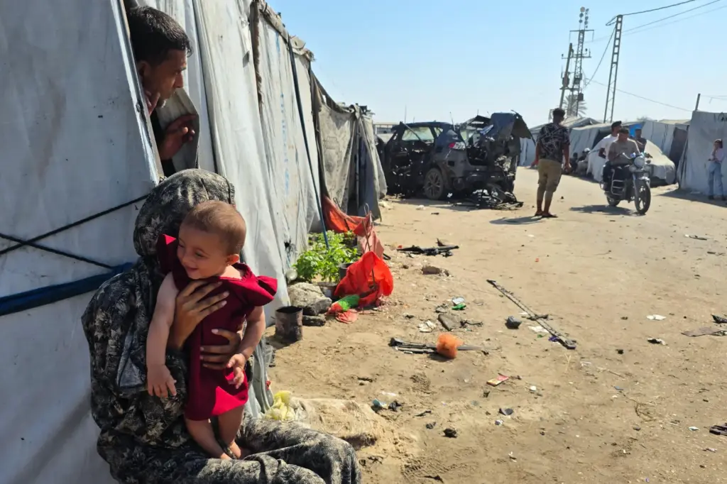 Palestinians look at a destroyed car following an Israeli military strike.