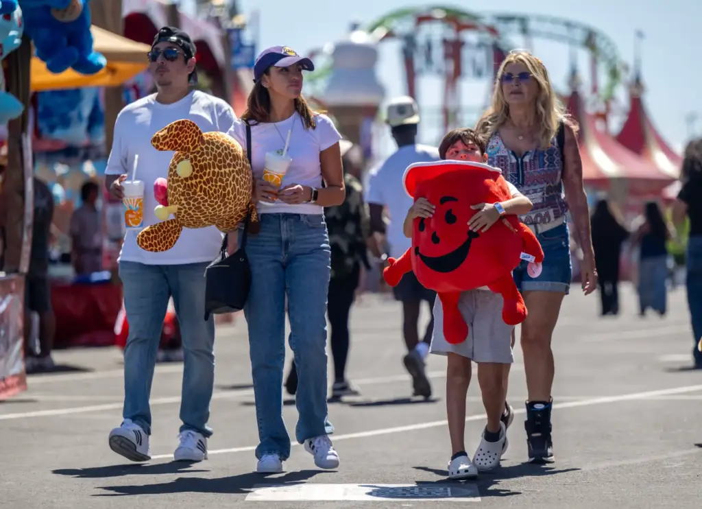 Fairgoers carry their stuffed game winnings as they walk through...