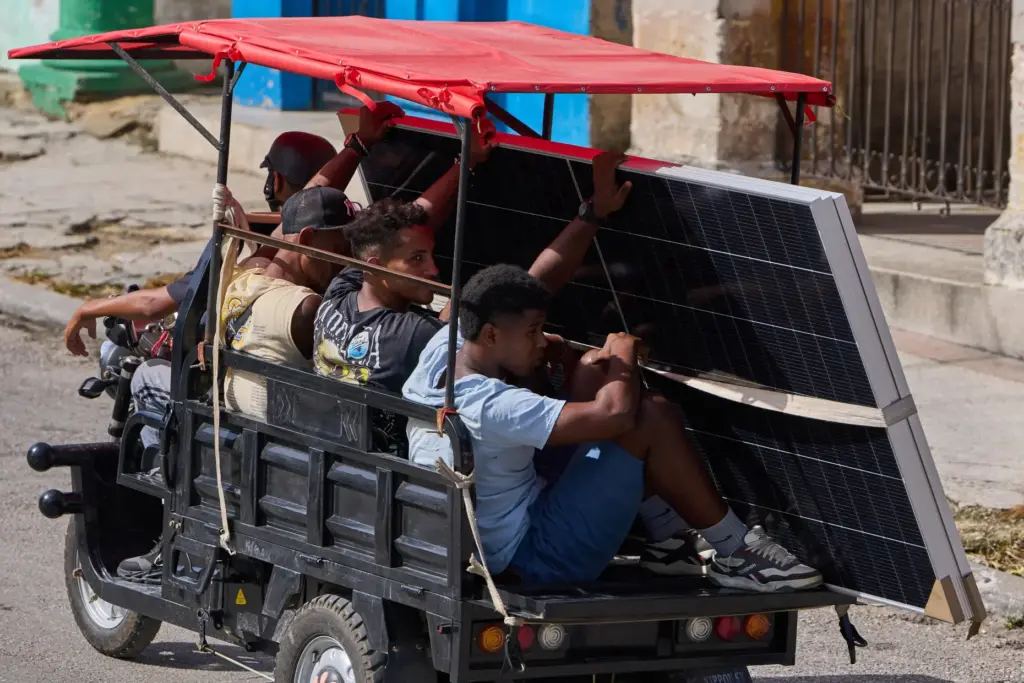 People transport solar panels on an electric tricycle in Havana,...