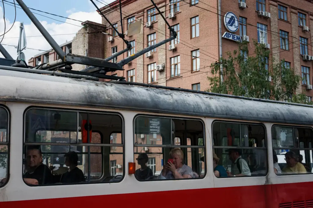 Commuters use the tram as they pass the Artem factory,...