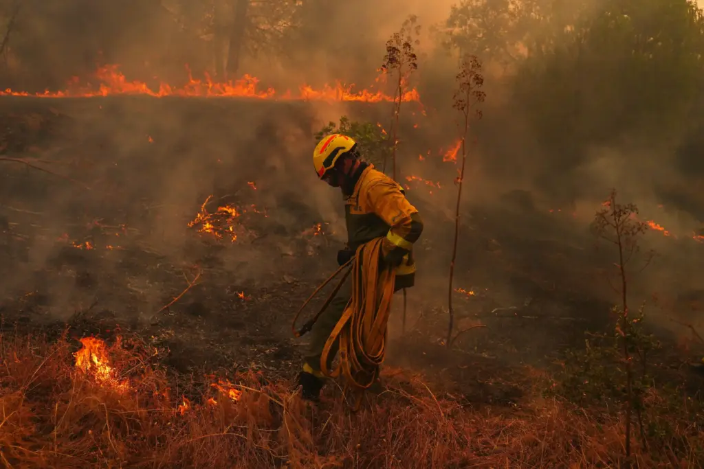 FILE – A firefighter carries a hose while battling a...
