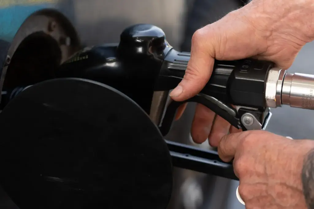 A person secures the fuel nozzel while filling up their tank.