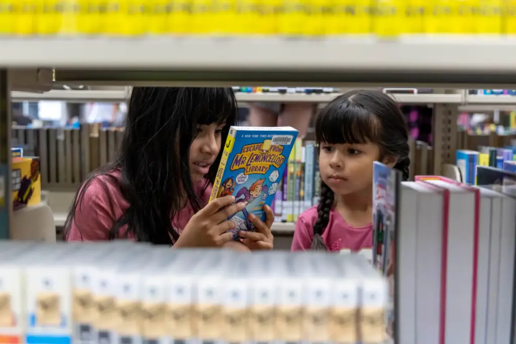 Yareli Ceballos, 8, (left) reads the back of a book...