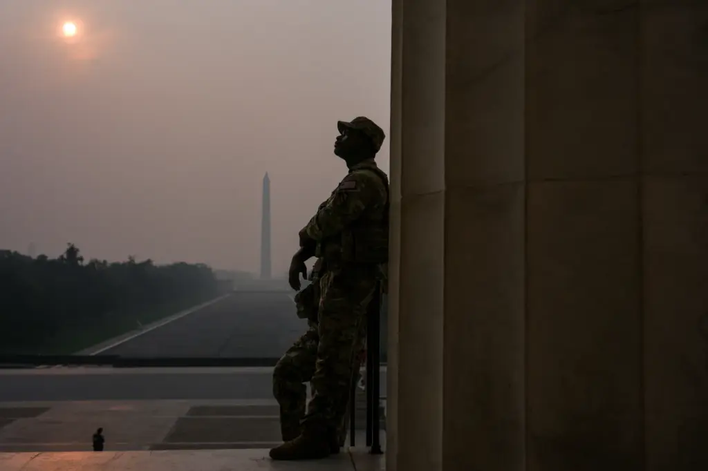 National Guardsmen patrol the Lincoln Memorial as the sun, obscured by wildfire smoke, rises.