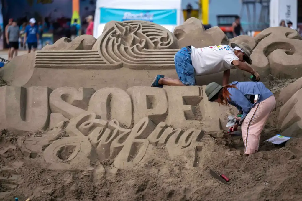 Sand sculptors carve the US Open of Surfing logo into...