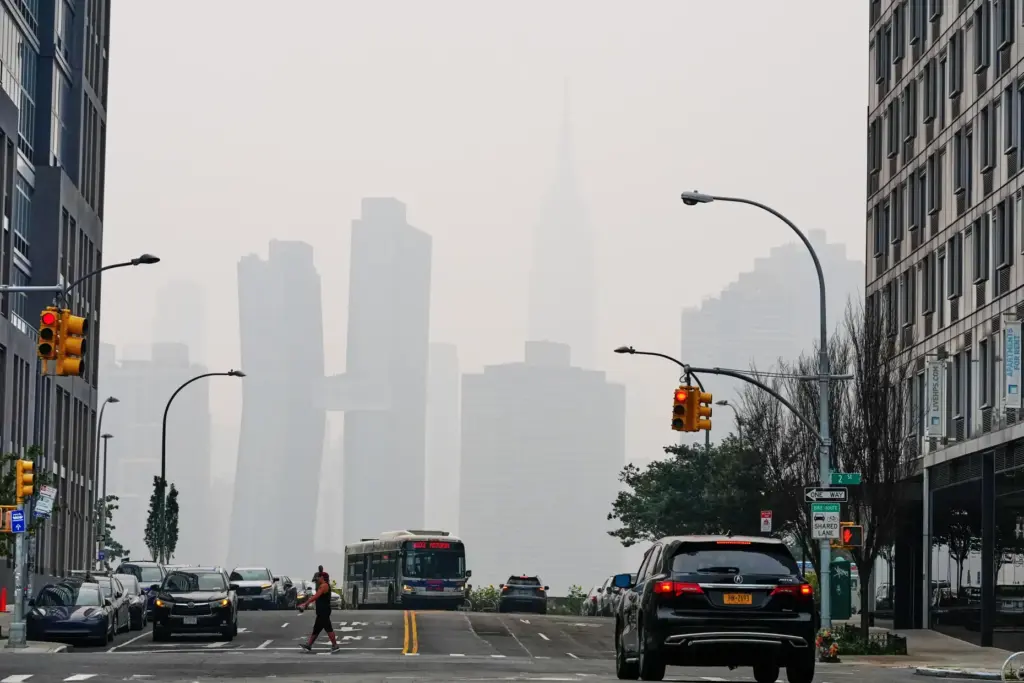 Pedestrians cross Borden Avenue as the New York City skyline is obscured in smoke.