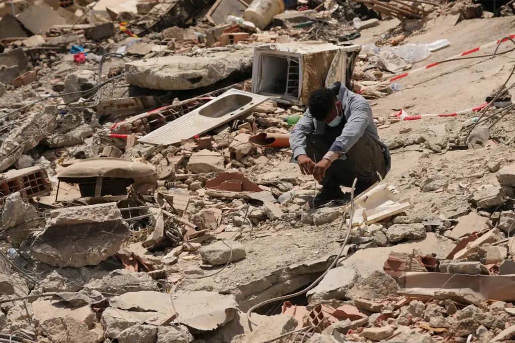 FILE – A man sits amid earthquake rubble in La...