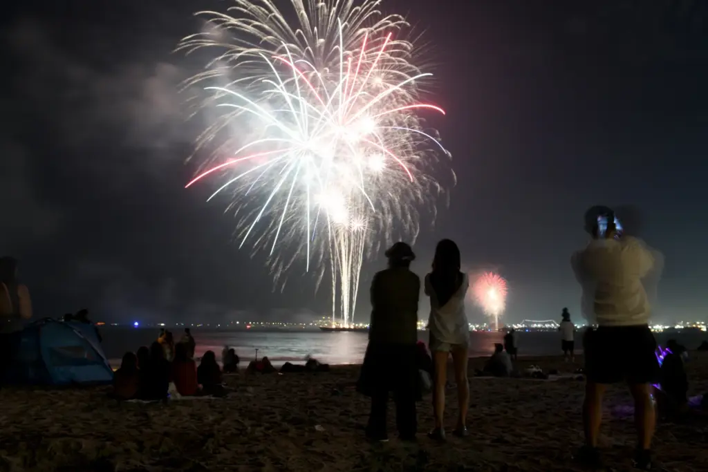 People watch simultaneous fireworks displays from Junipero Beach in Long...