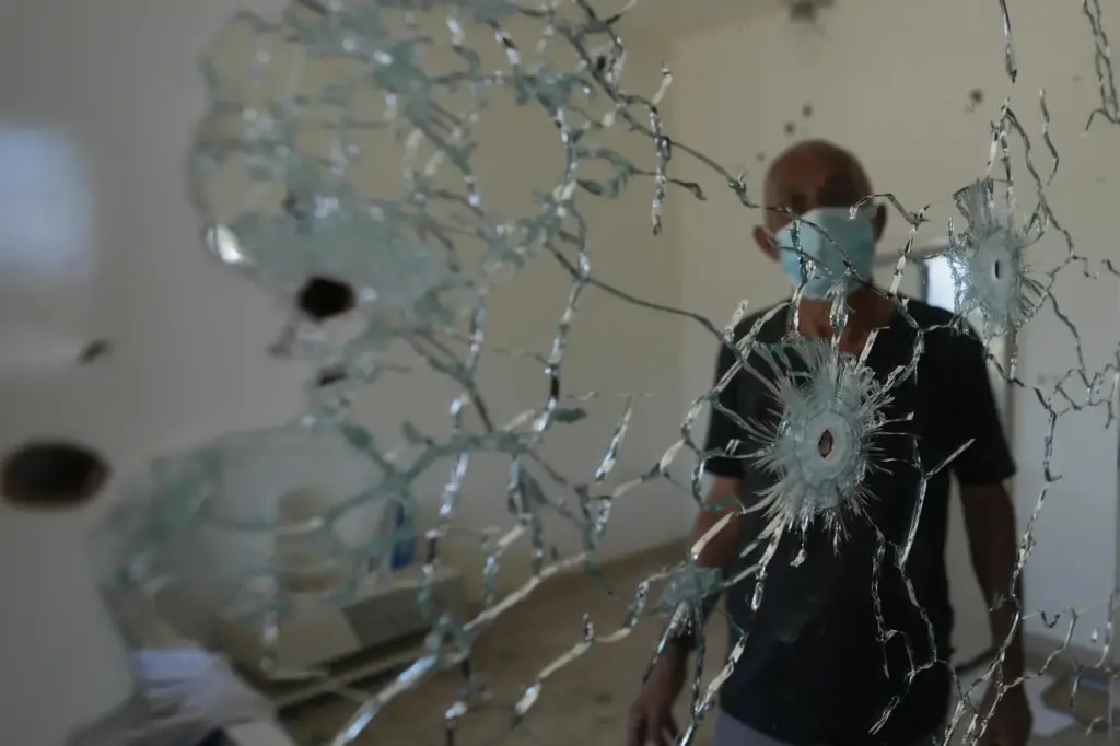 A resident stands behind a mirror riddled with bullet holes inside his home.