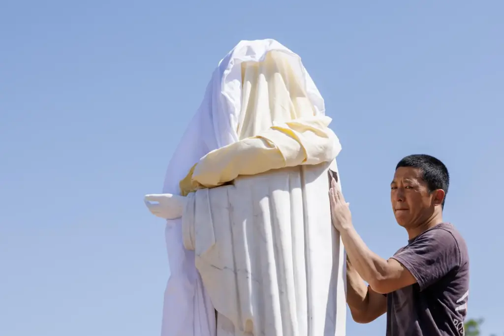 Volunteer cleans the vandalized statue of the Virgin Mary, which...