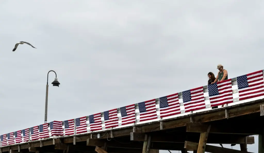 People look over the flag-covered railing on the pier in...