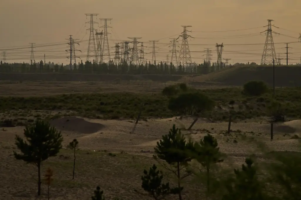 Electric pylons are seen in the horizon along sand dunes...