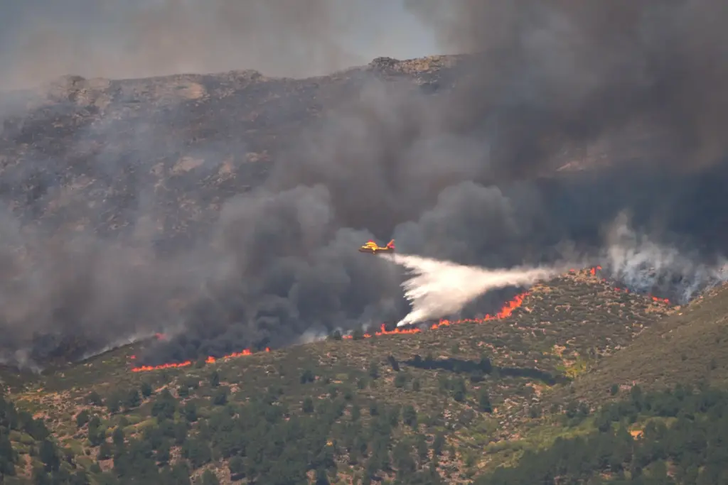 A seaplane drops water onto the fire as a wildfire...