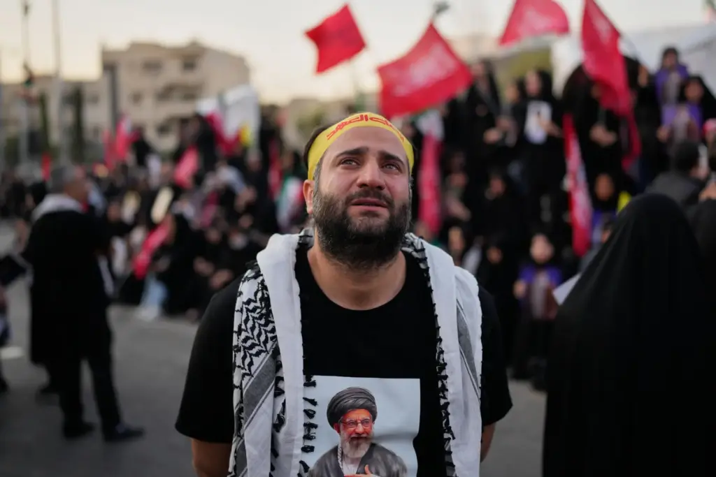 A mourner wearing a shirt depicting Iranian Supreme Leader Ayatollah Ali Khamenei weeps.