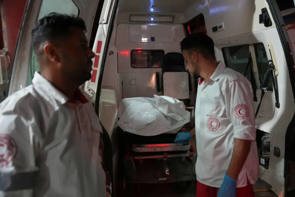 Palestinian paramedics stand at the back of an ambulance with a body.