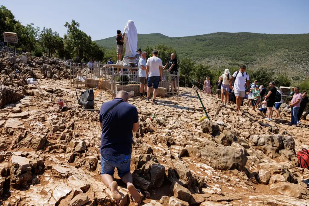 Pilgrims pray next to the vandalized statue of the Virgin...