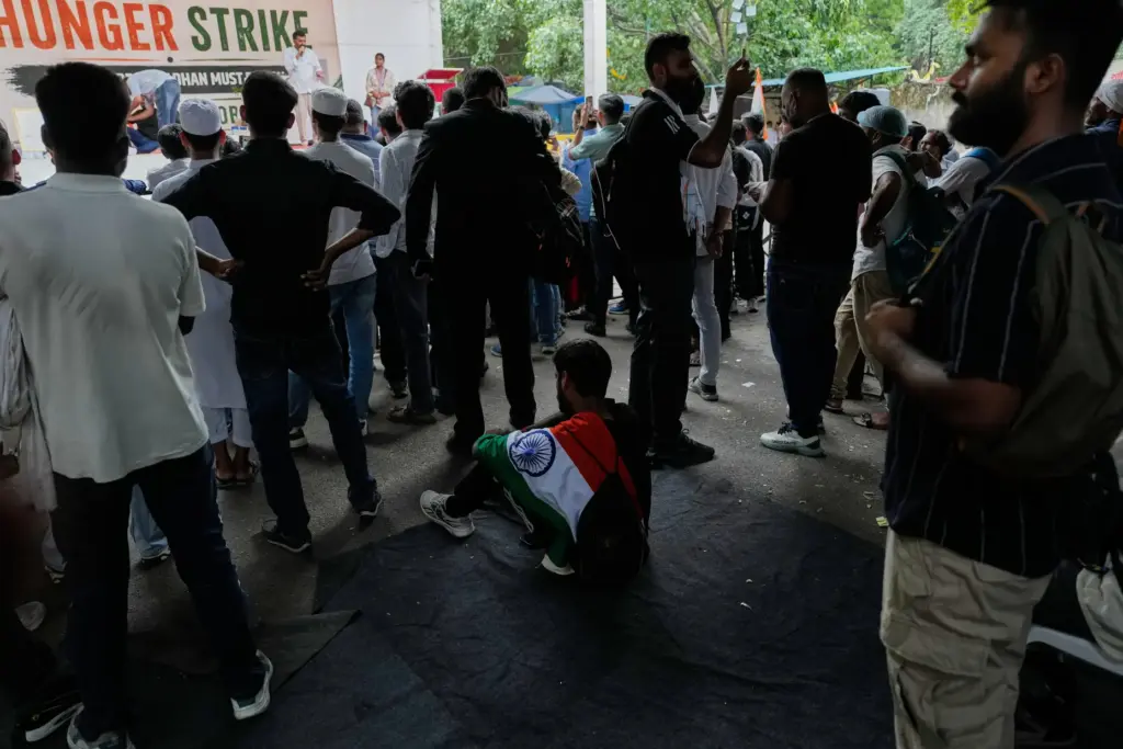A supporter with Indian flag on his shoulder sits and listens to a speaker.