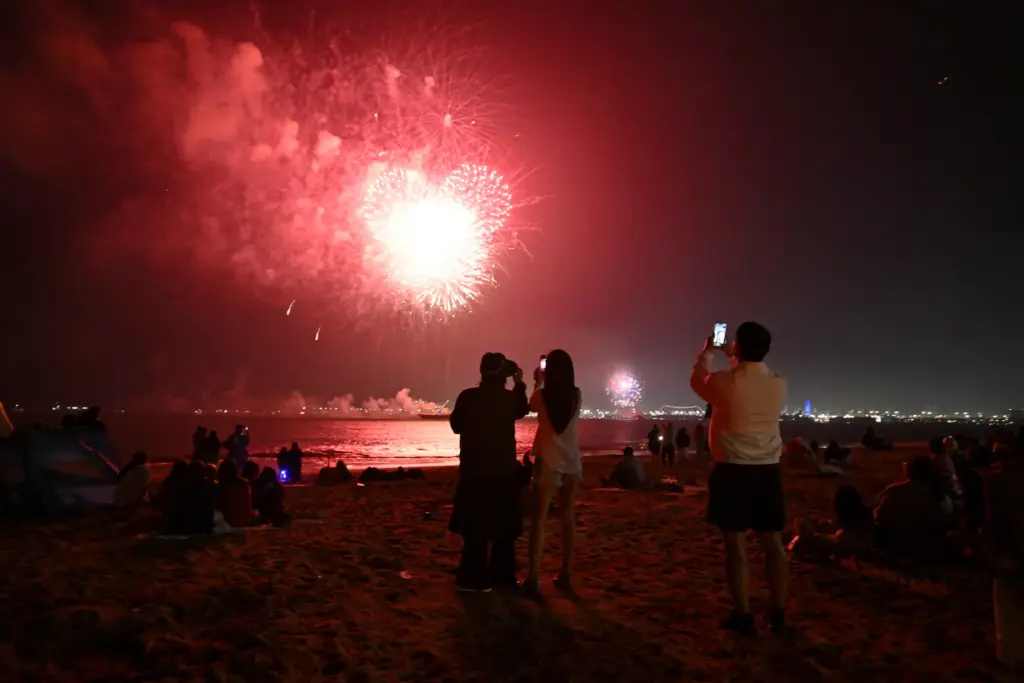 People watch simultaneous fireworks displays from Junipero Beach in Long...