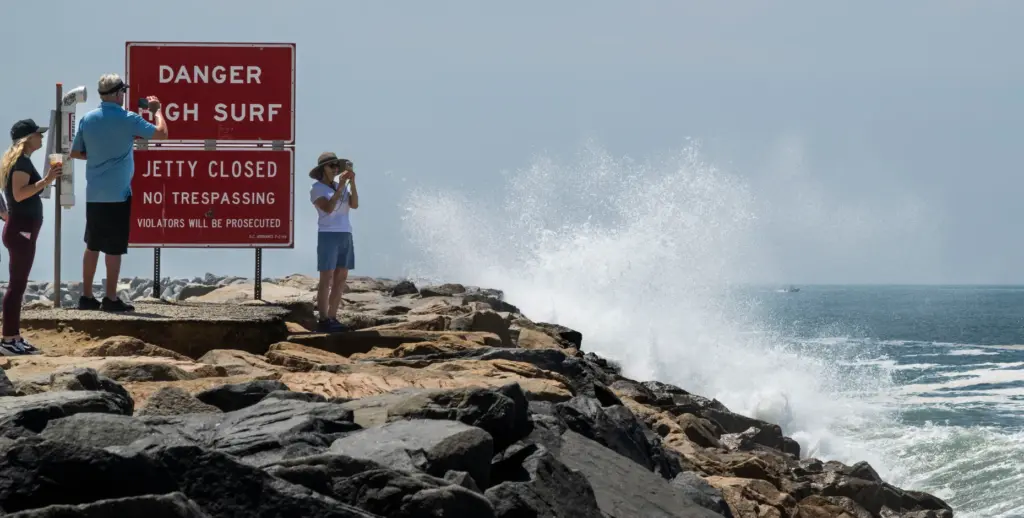 People take photos as waves crash off the jetty in...