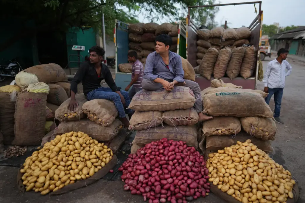 Laborers sit beside sacks of potatoes at a vegetable market...