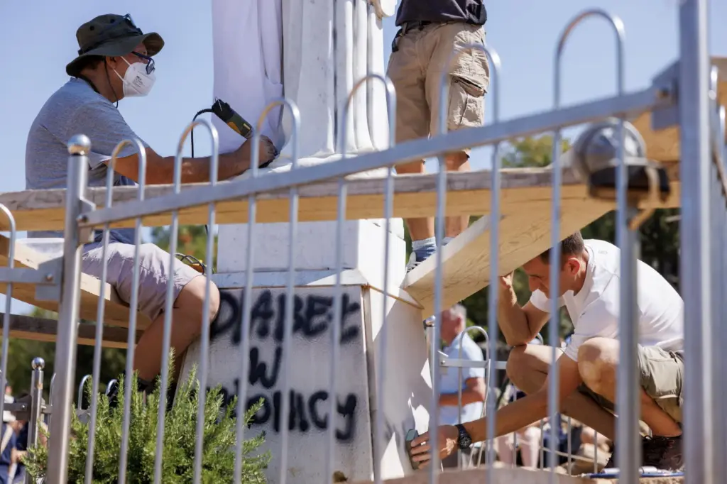 Volunteers clean the vandalized statue of the Virgin Mary, which...