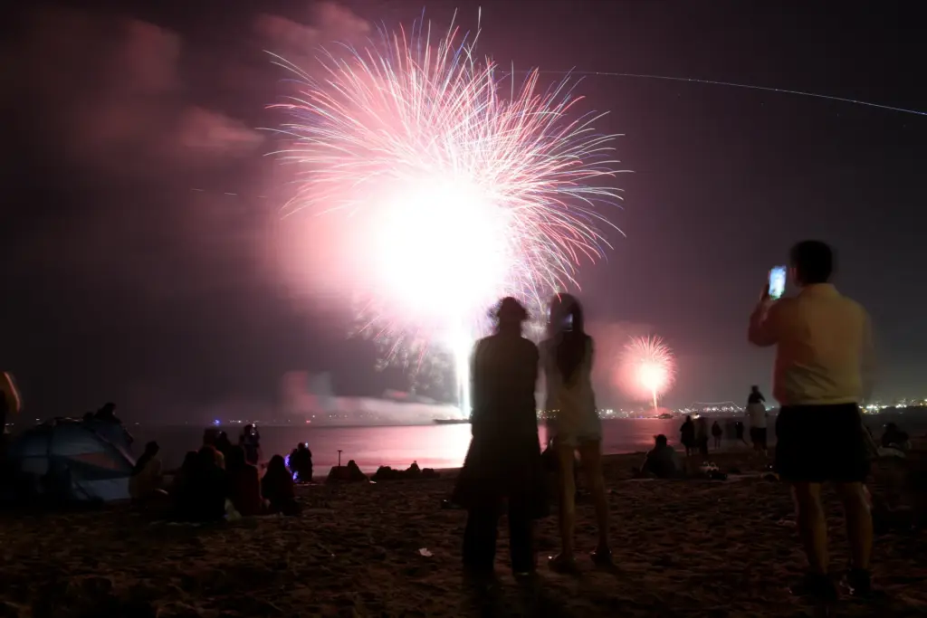 People watch simultaneous fireworks displays from Junipero Beach in Long...