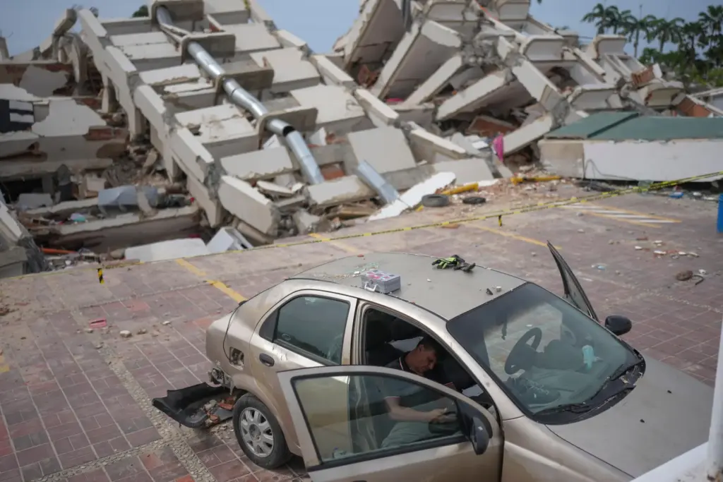 A volunteer helping remove debris from buildings damaged by the earthquakes rests on a damaged car.