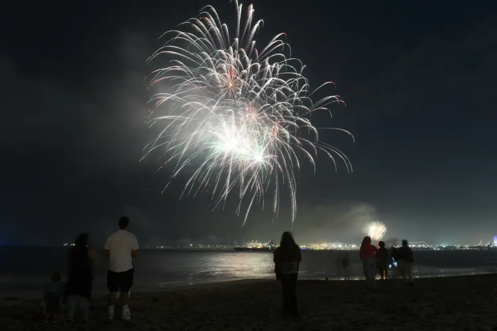 People watch simultaneous fireworks displays from Junipero Beach in Long...