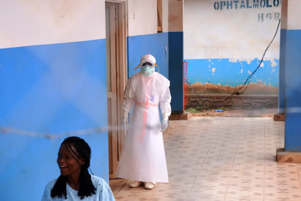 A health worker, wearing protective gear, stands outside the Ebola...