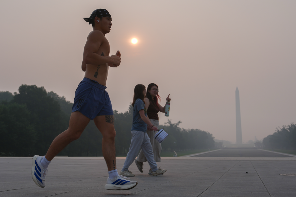 The sun is obscured by wildfire smoke as people run in front of the Washington Monument.