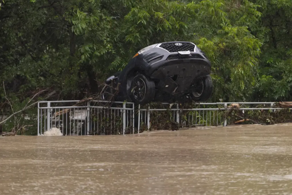 A flood-damaged car hangs from a fence.