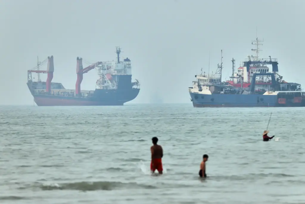 Children wade in the water with cargo ships at anchor in the Strait of Hormuz.