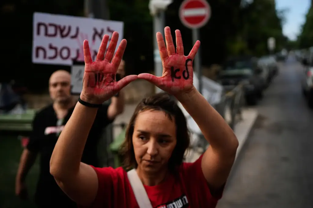 A woman holds up her hands, painted red to symbolize...