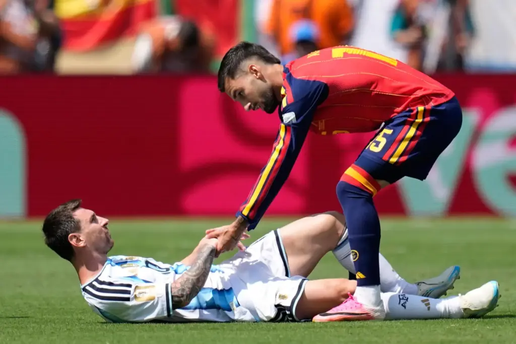 Spain’s Alex Baena helps Argentina’s Lionel Messi get back on...
