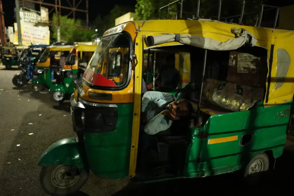 An auto-rickshaw driver rests inside his vehicle during a heat...