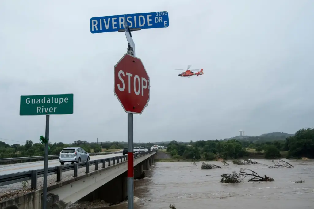 A helicopter flies over the Guadalupe River as floods pass...