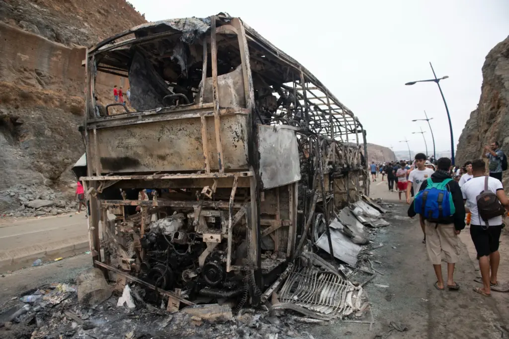 People walk past a burned bus.