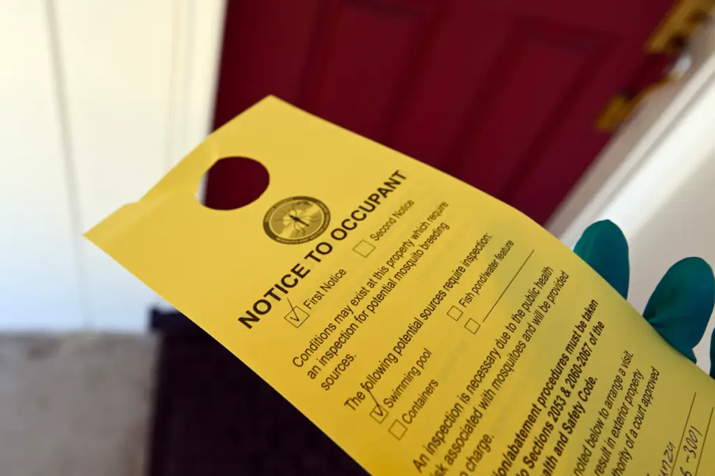 Vector Control Inspector Kevin Isunza look leaves a notice on...
