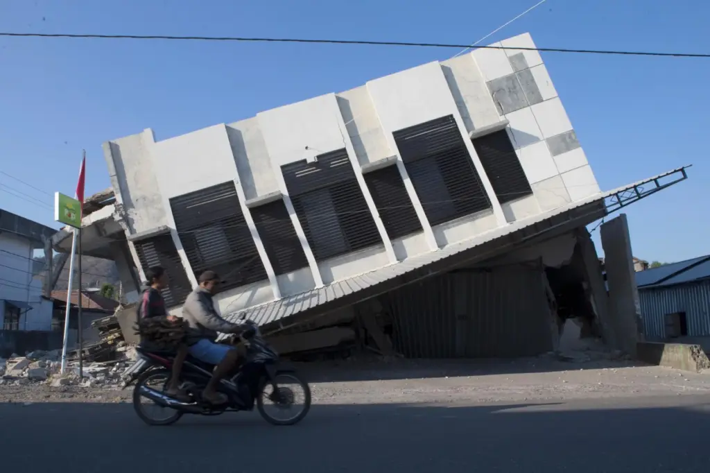 Motorists ride past a building that collapsed during an earthquake...
