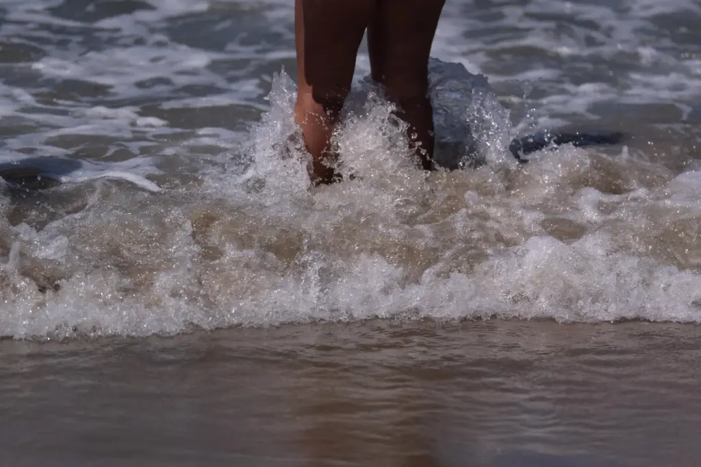 FILE – A beachgoer stands in shallow water at Bolsa...