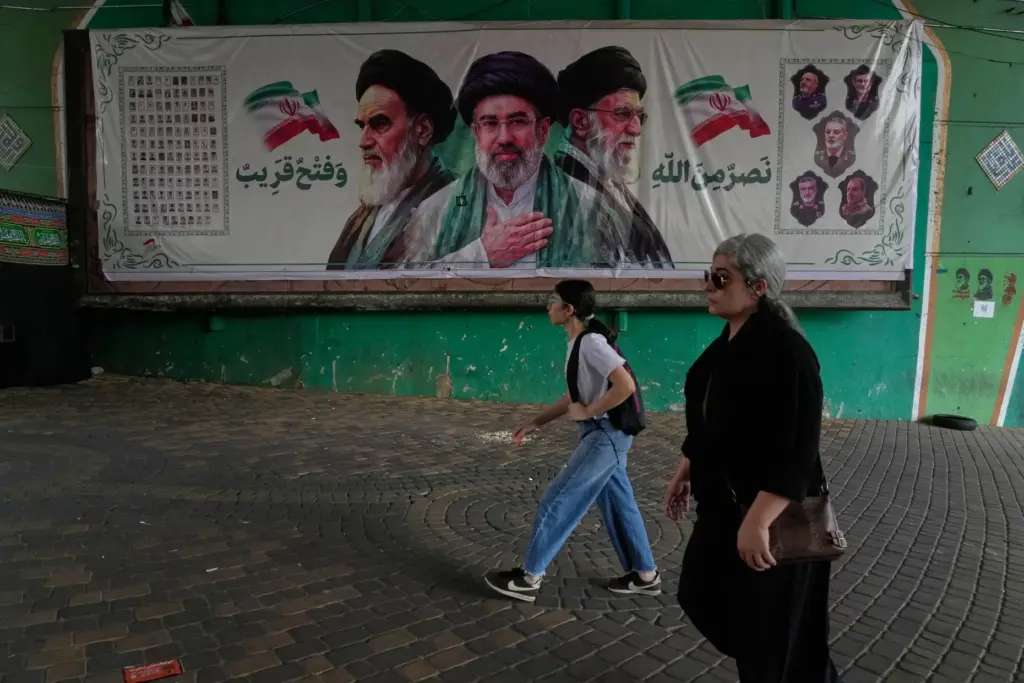 Women walk past a banner of Ayatollah Khomeini, Ayatollah Mojtaba Khamenei and Ayatollah Ali Khamenei.