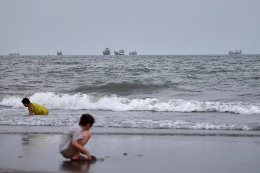 Children play at a beach as commercial vessels are anchored in the Strait of Hormuz.
