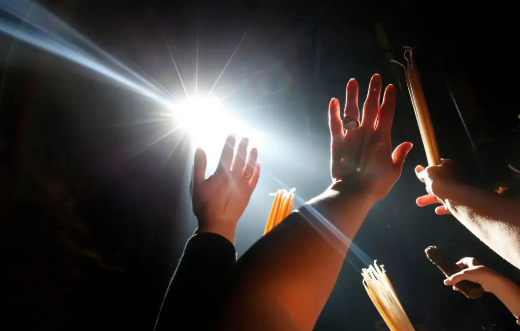 Christian Orthodox pilgrims raise their hands toward a beam of light.